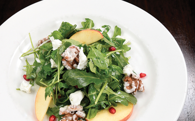 Green leafy salad with apple slices, walnuts, cheese crumbles, and pomegranate seeds on a white plate